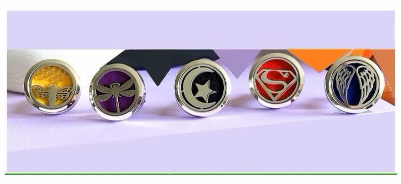 May include: Five silver car air freshener medallions with different designs. The designs include a dragonfly, a crescent moon with a star, a Superman logo, a butterfly, and a pair of angel wings.