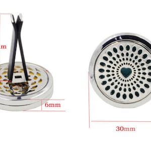 May include: Silver car air freshener with a black clip. The front of the air freshener has a green and silver design with a heart in the center. The air freshener measures 3 inches in diameter.