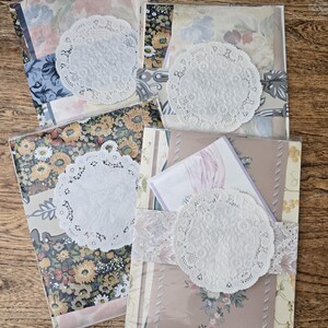 May include: Four bundles of patterned paper, each wrapped with a lace ribbon and a white paper doily. The paper features floral and vintage designs in various colors, including blue, pink, and yellow. The bundles are arranged on a wooden surface.