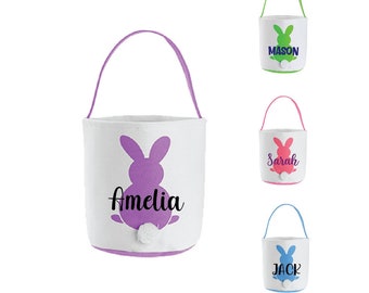 Puede incluir: Tres cestas de Pascua con orejas de conejo y una cola esponjosa. Las cestas son blancas con ribetes morados, rosas, azules y verdes. Las cestas están personalizadas con los nombres Amelia, Sarah, Jack y Mason.