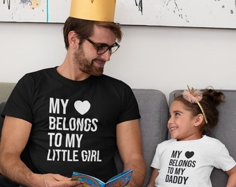 May include: A father and daughter wearing matching shirts. The father's shirt says "My heart belongs to my little girl" and the daughter's shirt says "My heart belongs to my daddy".