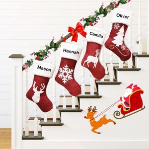 Può includere: Quattro calze di Natale rosse e bianche con i nomi "Mason", "Hannah", "Camila" e "Oliver" appese a un corrimano bianco. Una slitta rossa con una figura di Babbo Natale è sul muro con una renna che tira la slitta.