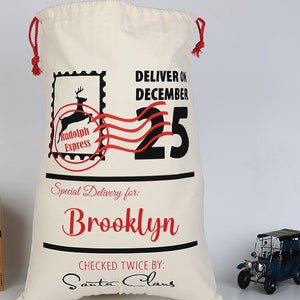 Pu&ograve; includere: Un sacco di Babbo Natale in tela bianca con cordoncino rosso, che presenta una grafica in nero e rosso di una renna con il testo "Rudolph Express" e "Deliver on December 25". Il sacco &egrave; personalizzato con il nome "Brooklyn" e il testo "Checked Twice By: Santa Claus".