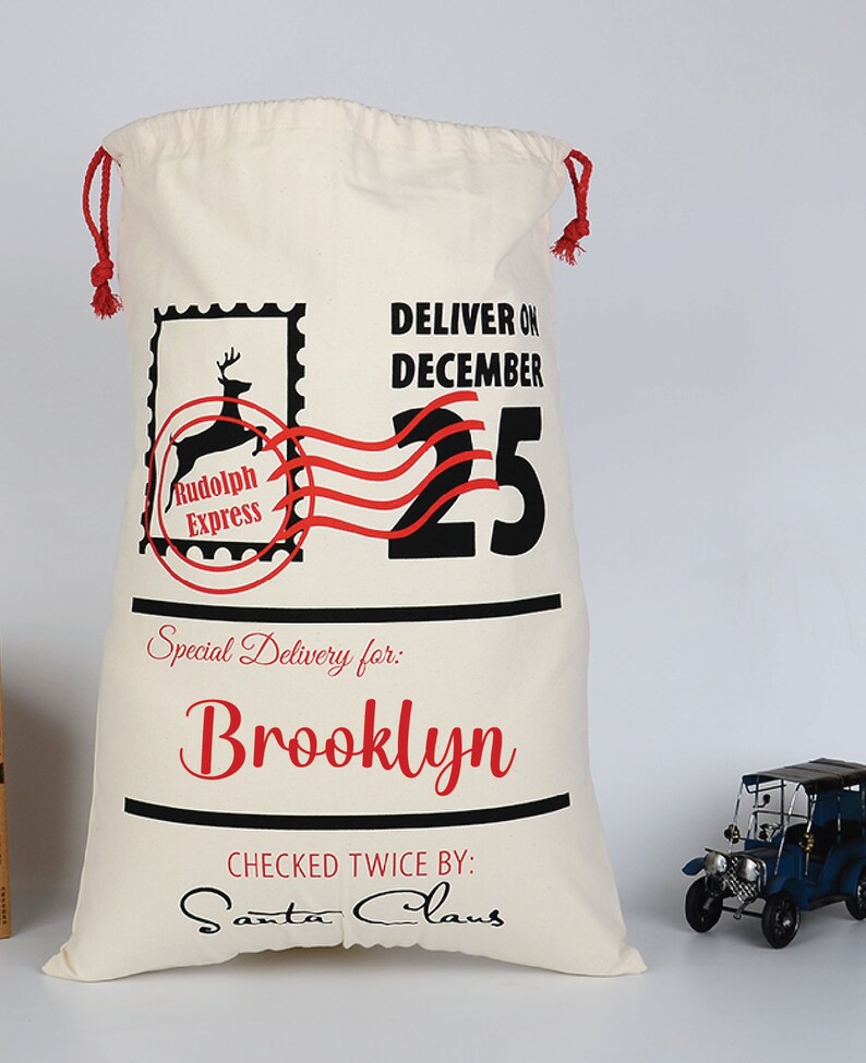 Pu&ograve; includere: Un sacco di Babbo Natale in tela bianca con cordoncino rosso, che presenta una grafica in nero e rosso di una renna con il testo "Rudolph Express" e "Deliver on December 25". Il sacco &egrave; personalizzato con il nome "Brooklyn" e il testo "Checked Twice By: Santa Claus".