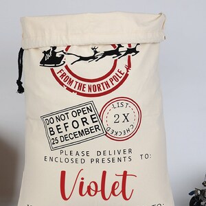 Pu&ograve; includere: Un sacco di Babbo Natale in tela bianca con un design rosso e nero. Il sacco ha una chiusura a coulisse e dice "From the North Pole" in un cerchio rosso. Dice anche "Do Not Open Before 25 December" e "Please Deliver Enclosed Presents To: Violet".