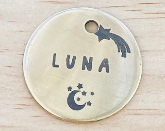 Könnte beinhalten: Ein runder, goldfarbener Metallschild mit dem Namen "LUNA" eingraviert. Das Schild zeigt einen Halbmond mit Sternen und einen Sternschnuppen.