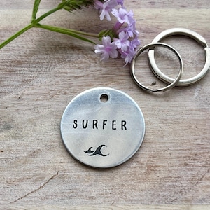 May include: Silver keyring with a round tag that says "SURFER" with a wave graphic.