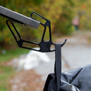 Może przedstawiać: Czarny metalowy hak przymocowany do metalowego pręta z wiszącym czarnym paskiem.