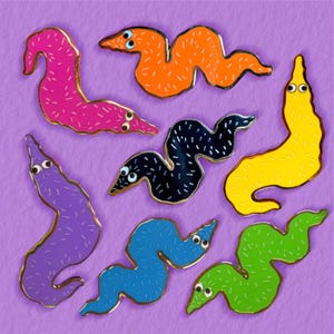 May include: A collection of seven enamel pins shaped like wiggly worms in various colors including pink, orange, yellow, black, purple, blue, and green. Each worm features two small white eyes with black pupils and a textured surface pattern.