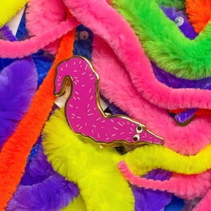 May include: A pink fuzzy worm pin with googly eyes, surrounded by colourful fuzzy worm toys in a variety of colours, including purple, green, yellow, and orange.