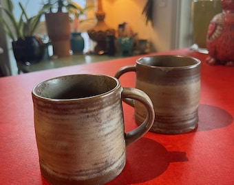 Conjunto de duas canecas de café artesanais em cerâmica com acabamento esmaltado em estilo rústico.