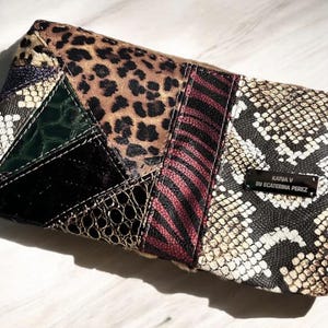 May include: A rectangular patchwork clutch featuring various animal print patterns, including leopard, zebra, and snakeskin. The clutch has a zipper closure and a small metal tag with the text "KATIA V BY ECATERINA PEREZ".