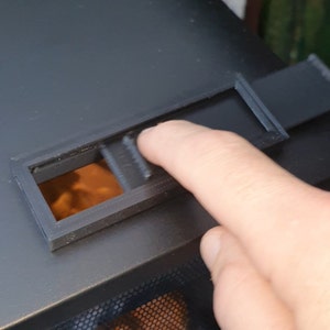 Könnte beinhalten: Ein schwarzer Metallkamin mit einem Maschensieb und einer kleinen rechteckigen Öffnung oben. Die Öffnung hat eine schwarze Plastikabdeckung, die zum Öffnen und Schließen geschoben werden kann.