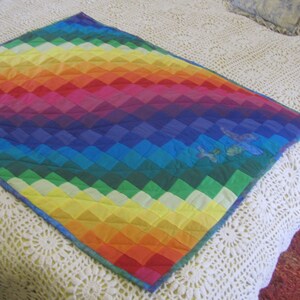 May include: A colourful rainbow quilt with a diamond pattern. The quilt is made of different shades of red, orange, yellow, green, blue, indigo, and violet.