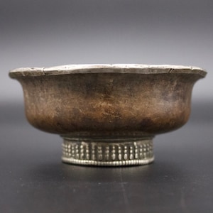May include: A silver bowl with a rounded base and a decorative rim. The bowl has a worn, aged appearance.