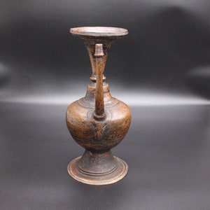 May include: An antique, brown metal pitcher with a wide, round base and a single spout. The pitcher has a worn, aged appearance.