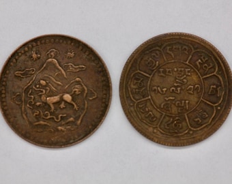 Puede incluir: Una moneda de cobre con un diseño de una criatura mítica en un lado y un diseño circular con escritura tibetana en el otro.