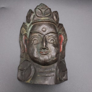 May include: A carved wooden mask of a deity with a crown of leaves, painted in shades of green, black, and red.