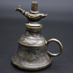 May include: An antique brass oil lamp with a bird-shaped spout and a handle. The lamp has a worn, aged finish.