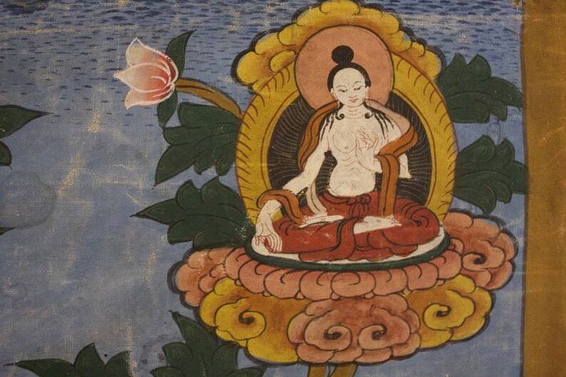 Puede incluir: Una pintura de una deidad sentada en posici&oacute;n de loto sobre una flor de loto. La deidad lleva una t&uacute;nica roja y tiene un cuerpo blanco. El fondo es azul y tiene un dise&ntilde;o floral.