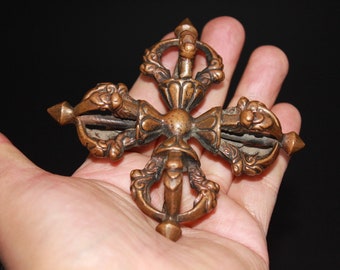 May include: A four-armed, bronze-colored, ornate, Tibetan prayer wheel with intricate details and a spinning mechanism.