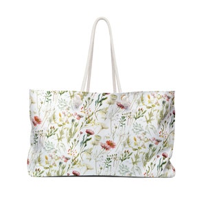 May include: A white canvas tote bag with a floral pattern featuring pink, red, and yellow flowers and green leaves. The bag has white rope handles.