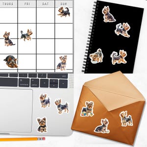 various dog stickers on a laptop keyboard, a spiral-bound notebook, and an envelope, all featuring small illustrations of dogs.
