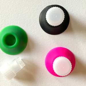 May include: Three silicone suction cups in green, black, and pink with white plastic tops. A separate white plastic top is also shown.
