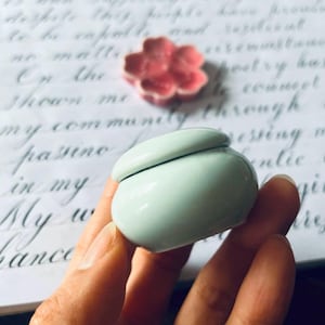 May include: A small, light blue ceramic jar with a lid. The jar is round and has a smooth, glossy finish.