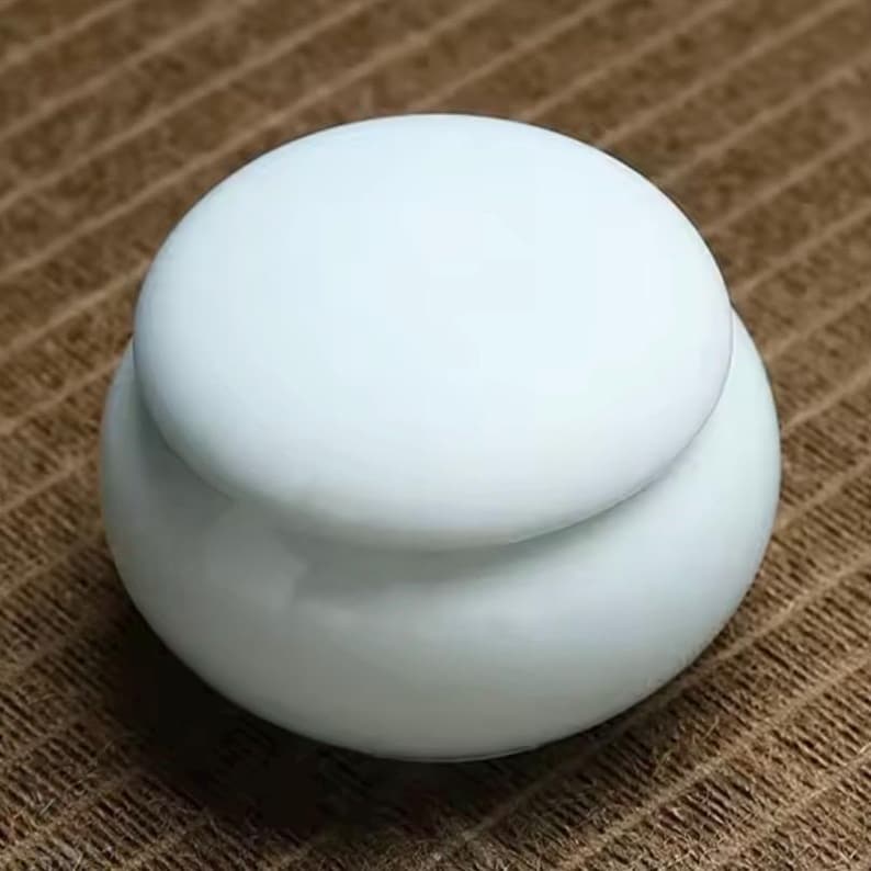 May include: A small, round, light blue ceramic jar with a lid. The jar has a smooth, glossy finish.
