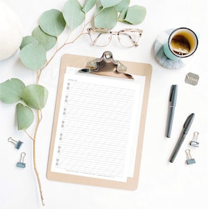 Puede incluir: Una composición en plano con un portapapeles marrón que contiene hojas de práctica de caligrafía. La imagen incluye gafas, bolígrafos, una taza de té y hojas de eucalipto. También hay pequeños clips y una etiqueta metálica.