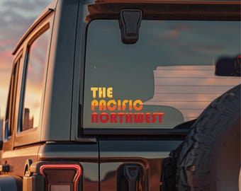 May include: A black SUV with a window decal that reads "THE PACIFIC NORTHWEST" in a gradient of yellow, orange, and red. The decal is on the rear window of the vehicle, with a spare tire visible.