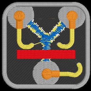 May include: A square embroidered patch featuring a dark gray background with a light gray border. The design depicts a central Y-shaped element in blue and yellow, a horizontal red bar, and three circular gray components with yellow and orange accents.