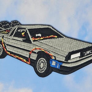 May include: A gray embroidered patch of the DeLorean time machine from the movie Back to the Future. The car is flying with flames coming out of the back. The car has the text "DMC" on the back.