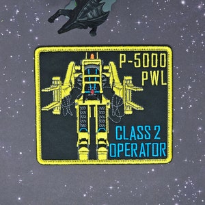 May include: Yellow and black embroidered patch with a robot-like figure in the center. The text "P-5000 PWL CLASS 2 OPERATOR" is printed on the patch.