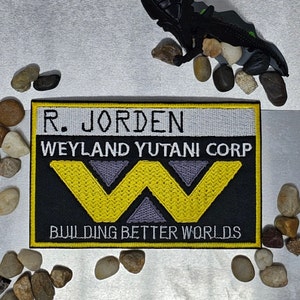 May include: Black and yellow embroidered patch with the text "R. Jorden Weyland Yutani Corp Building Better Worlds".