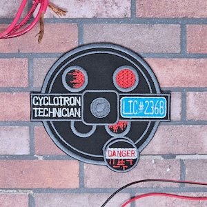 May include: A black and gray embroidered patch with the text "Cyclotron Technician" and "LTC #2368". The patch also features a red and gray design with the word "Danger" in Japanese.