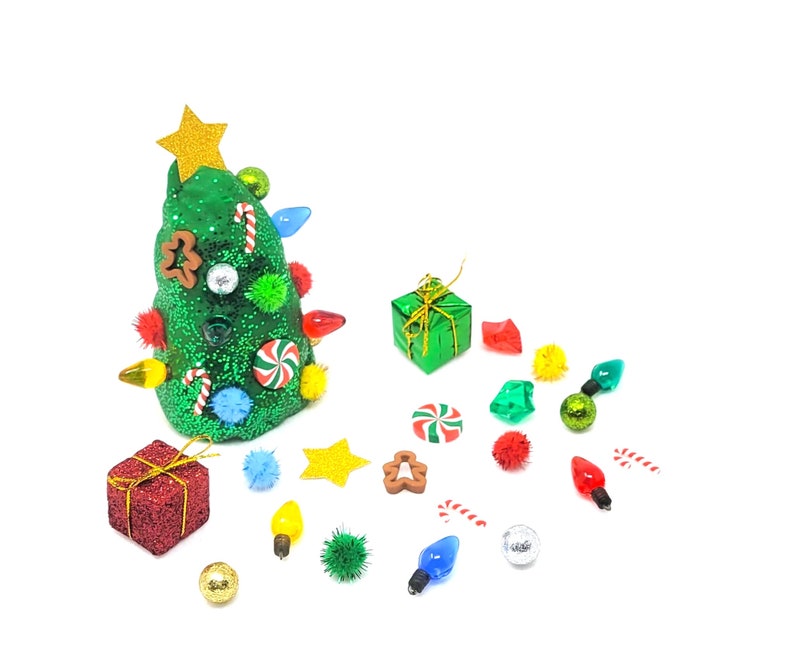 Puede incluir: Un caprichoso &aacute;rbol de Navidad con una estrella dorada, adornado con luces de colores, caramelos y adornos. Acompa&ntilde;ando al &aacute;rbol hay regalos en miniatura, caramelos y elementos decorativos, todo sobre un fondo blanco.