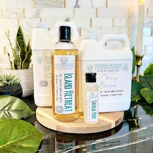 Könnte beinhalten: Eine Kollektion von Escential Elements Wäscheduft-Boostern, bestehend aus zwei großen weißen Kunststoffkanistern, einer durchsichtigen Flasche mit der Aufschrift Island Retreat und einer kleinen durchsichtigen Flasche mit der Aufschrift Dahlia Noir.