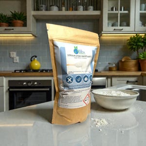 May include: A brown paper bag of "Sodium Percarbonate" with a white and blue label, next to a bowl of white powder. The bag has a logo and icons indicating it's a natural cleaner. The product is displayed on a kitchen countertop.