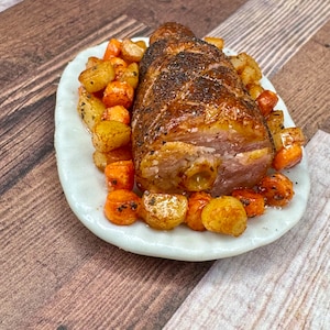 May include: A roasted meatloaf with a crispy brown crust served on a white plate with roasted potatoes and carrots.