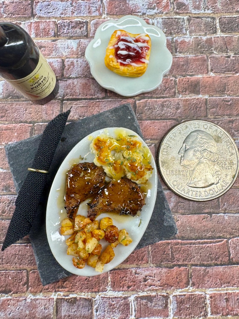 May include: A miniature plate with a meal of two small pieces of meat, mashed potatoes with gravy, and roasted potatoes. A small bottle of wine and a pastry with red jam are also pictured.