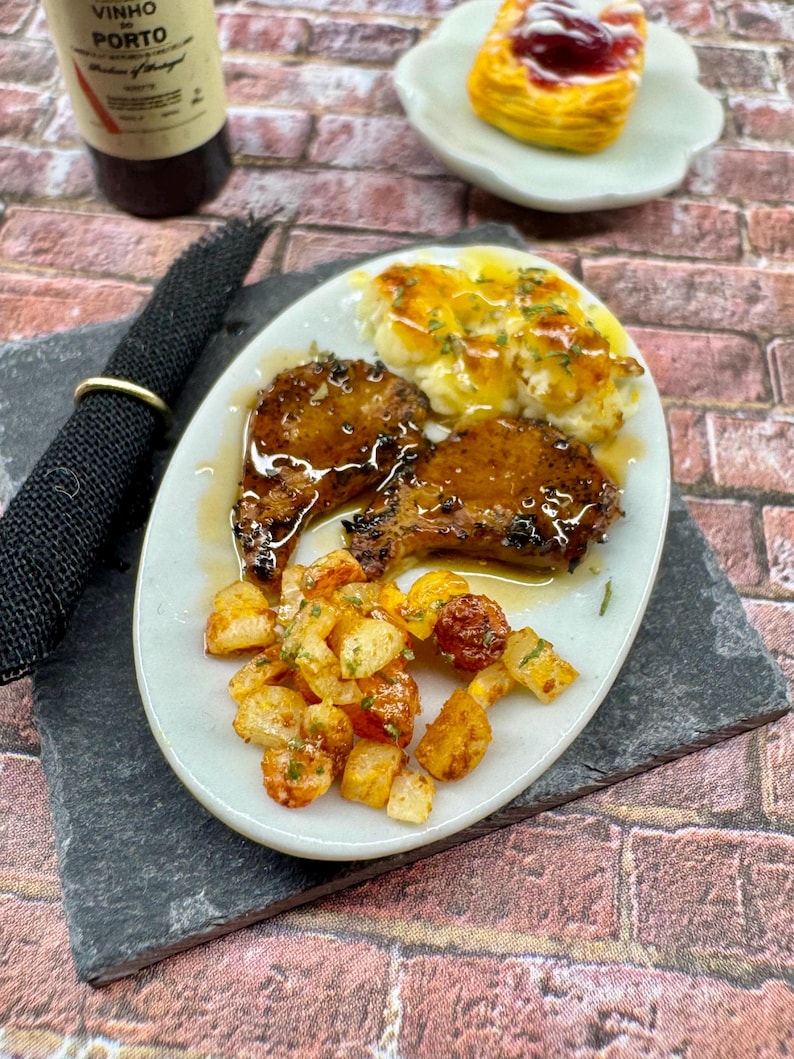 May include: A white plate with two pieces of grilled meat, a side of mashed potatoes with a brown sauce, and a side of roasted potatoes. The meat is glazed with a brown sauce and the potatoes are seasoned with herbs.