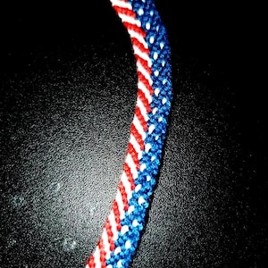 May include: A red, white, and blue friendship bracelet with a diagonal pattern.