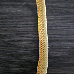 Puede incluir: Un brazalete de amistad amarillo y blanco hecho con cuerda trenzada.