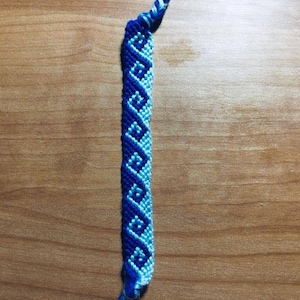 Peut inclure: Un bracelet d'amitié bleu et blanc avec un motif géométrique.