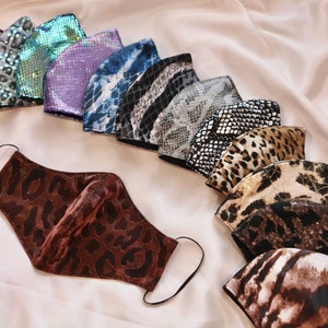 May include: A collection of face masks with various animal print designs, including leopard, snake, and zebra patterns. The masks are in shades of brown, black, white, and metallic colors. Each mask has black elastic ear loops and is displayed on a white surface.