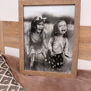 May include: Black and white drawing of two young girls laughing in a field. The girls are wearing dresses and have their hair pulled back. The drawing is framed in a light wood frame.