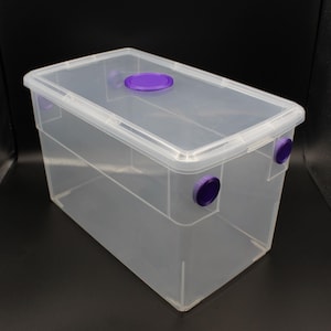 May include: A clear plastic storage box with a purple lid and two purple circles on the side. The box is empty.