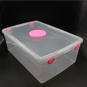 May include: Clear plastic storage box with a pink lid. The box has a pink latch on the side.
